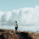Hiking Adventure - A person walking up a hill with clouds in the sky